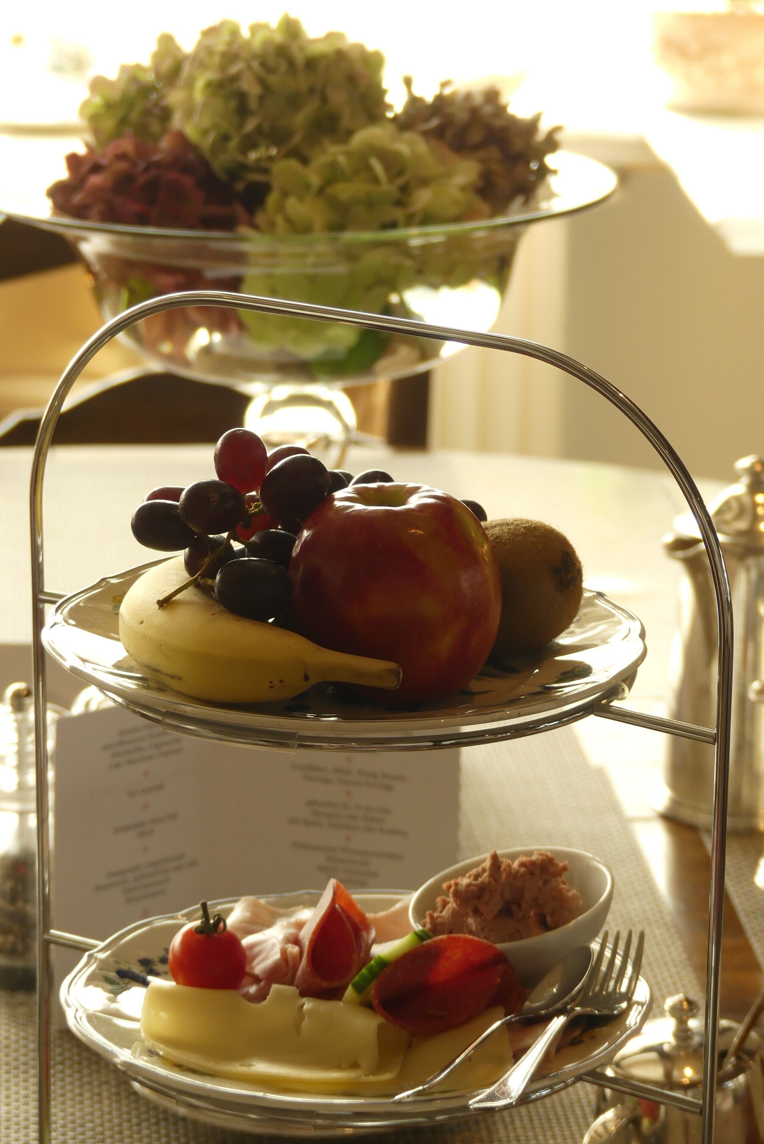 A three-tiered serving tray with various fruits and a small bowl of food, placed on a table with a menu in the background.