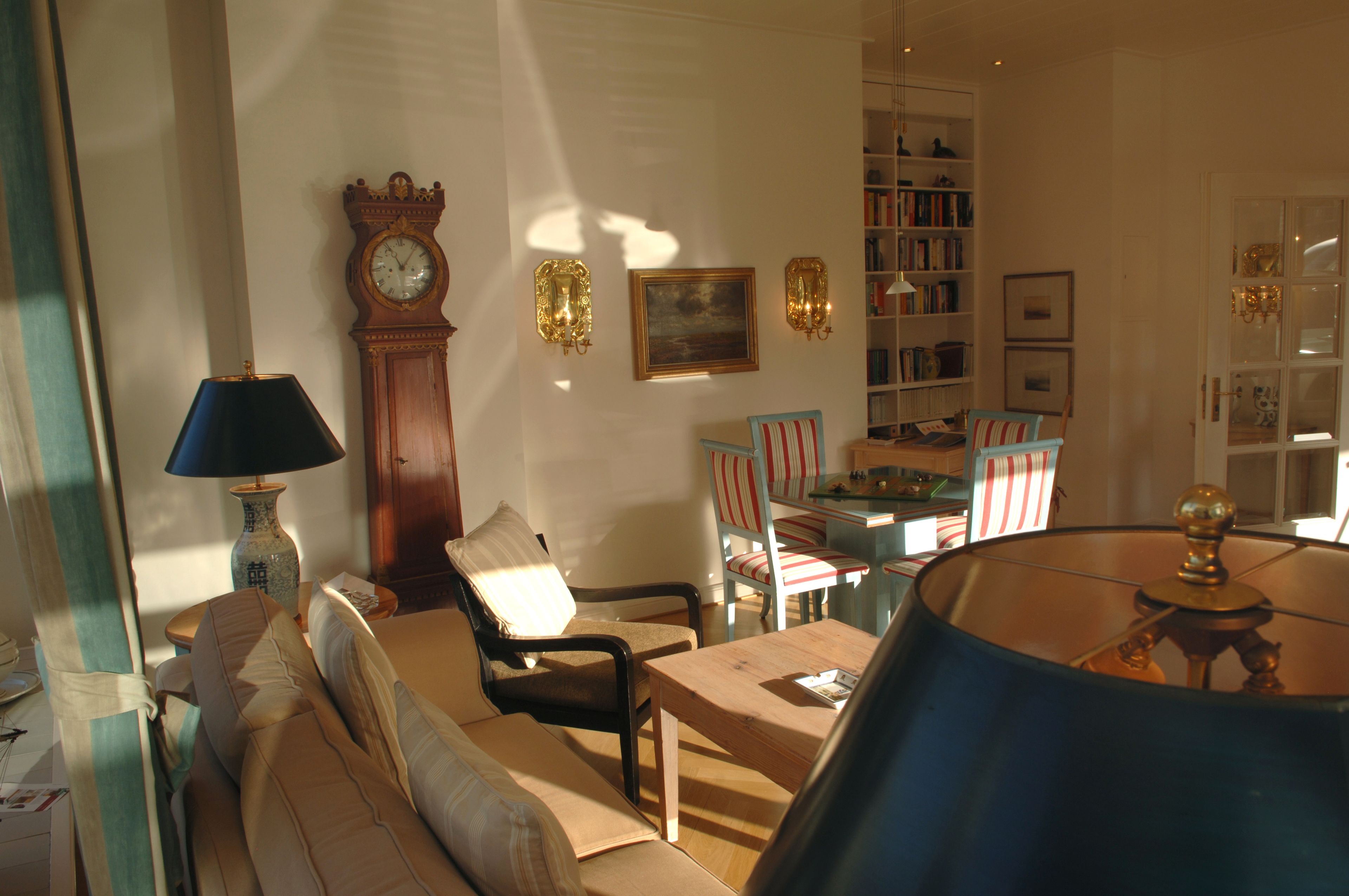 Ein Wohnzimmer mit einer Couch, Sesseln, einem Couchtisch, einer Lampe, einer Uhr, einem Gemälde und einem Bücherregal.