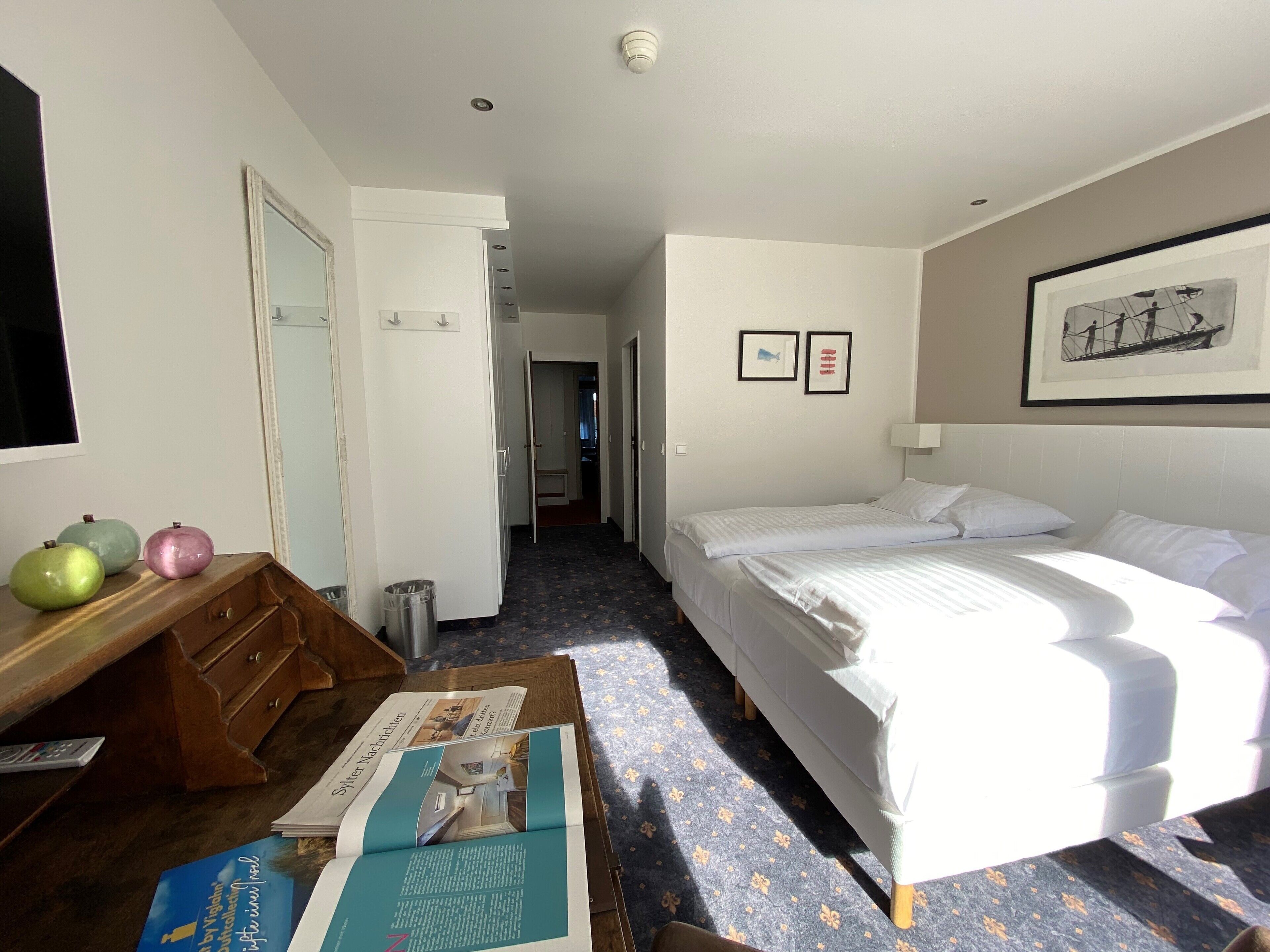 A hotel room with a bed, a desk with a chair, a trash bin, and a window.