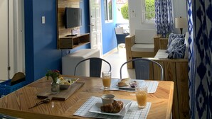 Ein Zimmer mit Esstisch, gedeckt für ein Frühstück, einem an der Wand befestigten Fernseher und Blick ins Freie durch eine geöffnete Tür.