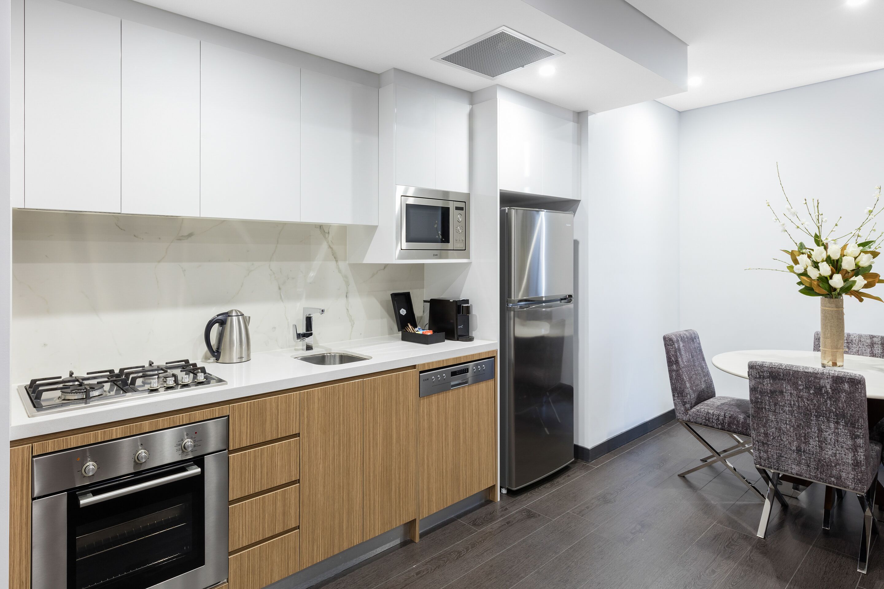 A modern kitchen with white cabinets, a built-in microwave, stainless steel appliances, and a dining area with a table and chairs.
