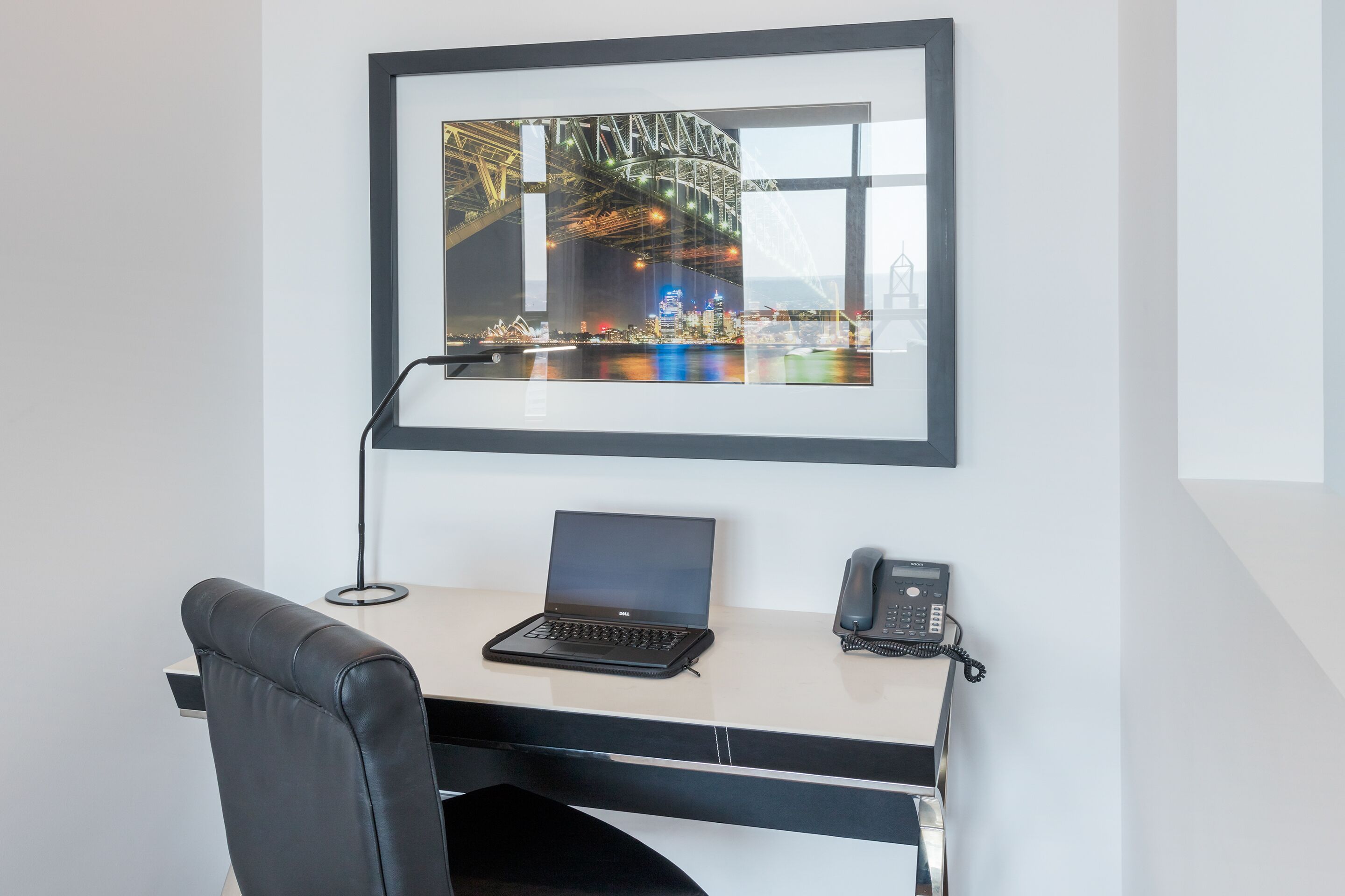 A modern office desk with a laptop, a telephone, and a framed picture of a bridge.