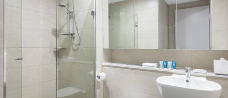 Un baño moderno con ducha envuelta en vidrio, un lavamanos blanco y un inodoro.