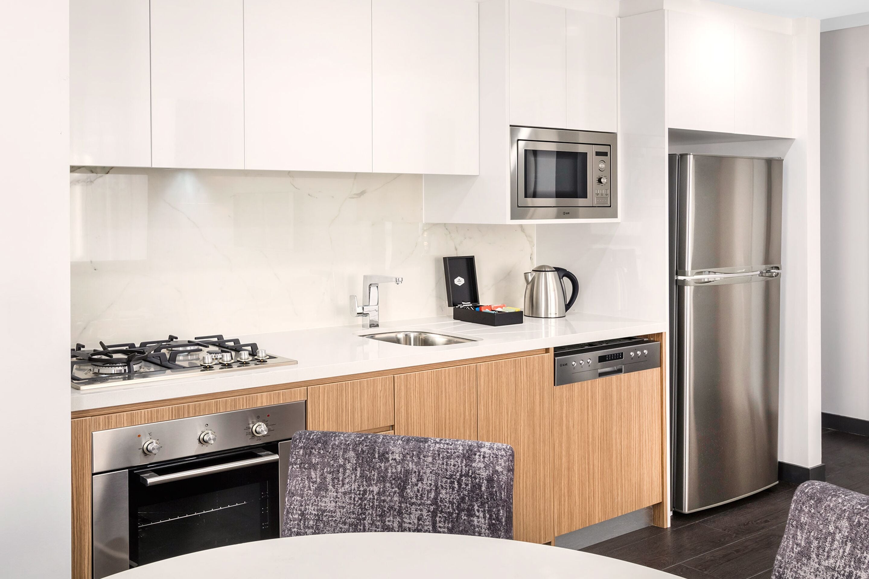 A modern kitchen with white cabinets, stainless steel appliances, a built-in microwave, a refrigerator, a gas stove, and a dishwasher.