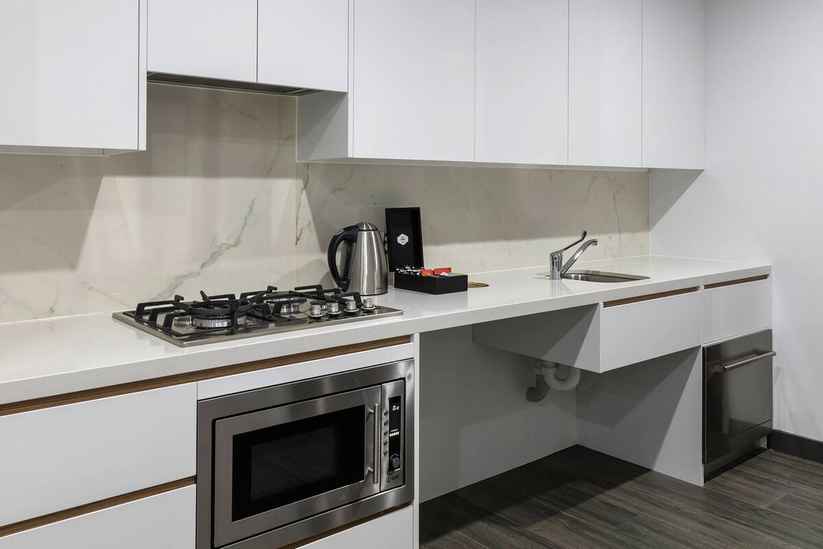 A modern kitchen with white cabinets, a stainless steel stove, an oven, a sink, and a marble backsplash.