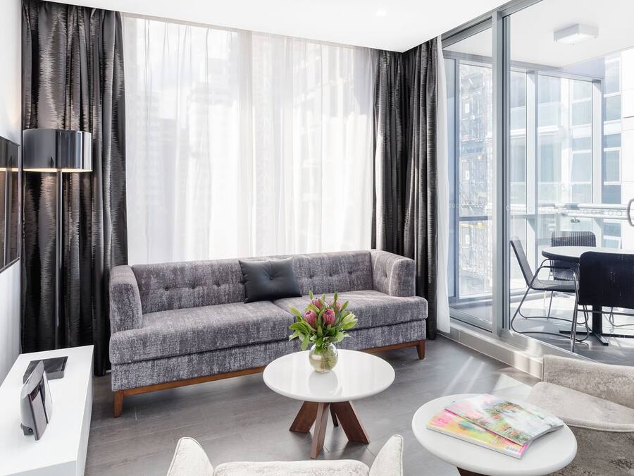Una sala moderna con un sofá gris, una mesita de centro blanca y un televisor sobre un mueble blanco.