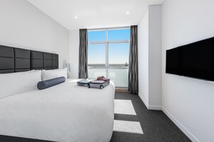 Habitación de hotel moderna con una cama grande, un televisor de pantalla plana, una ventana con cortinas y vistas al exterior.