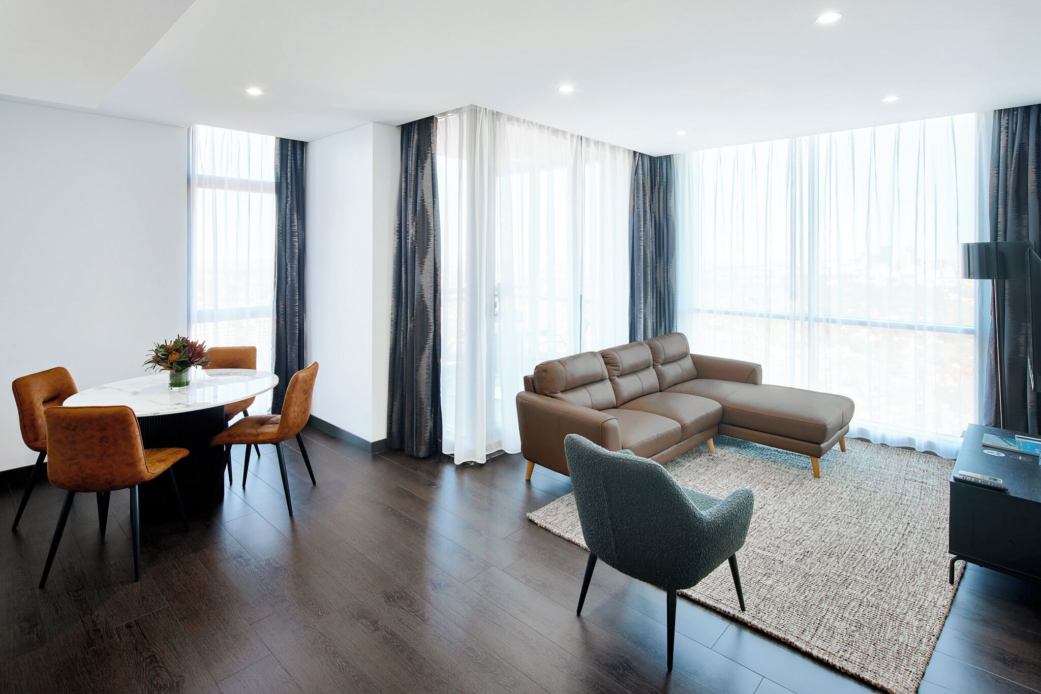 A modern living room with a brown leather sofa, a round dining table with chairs, and a TV stand.
