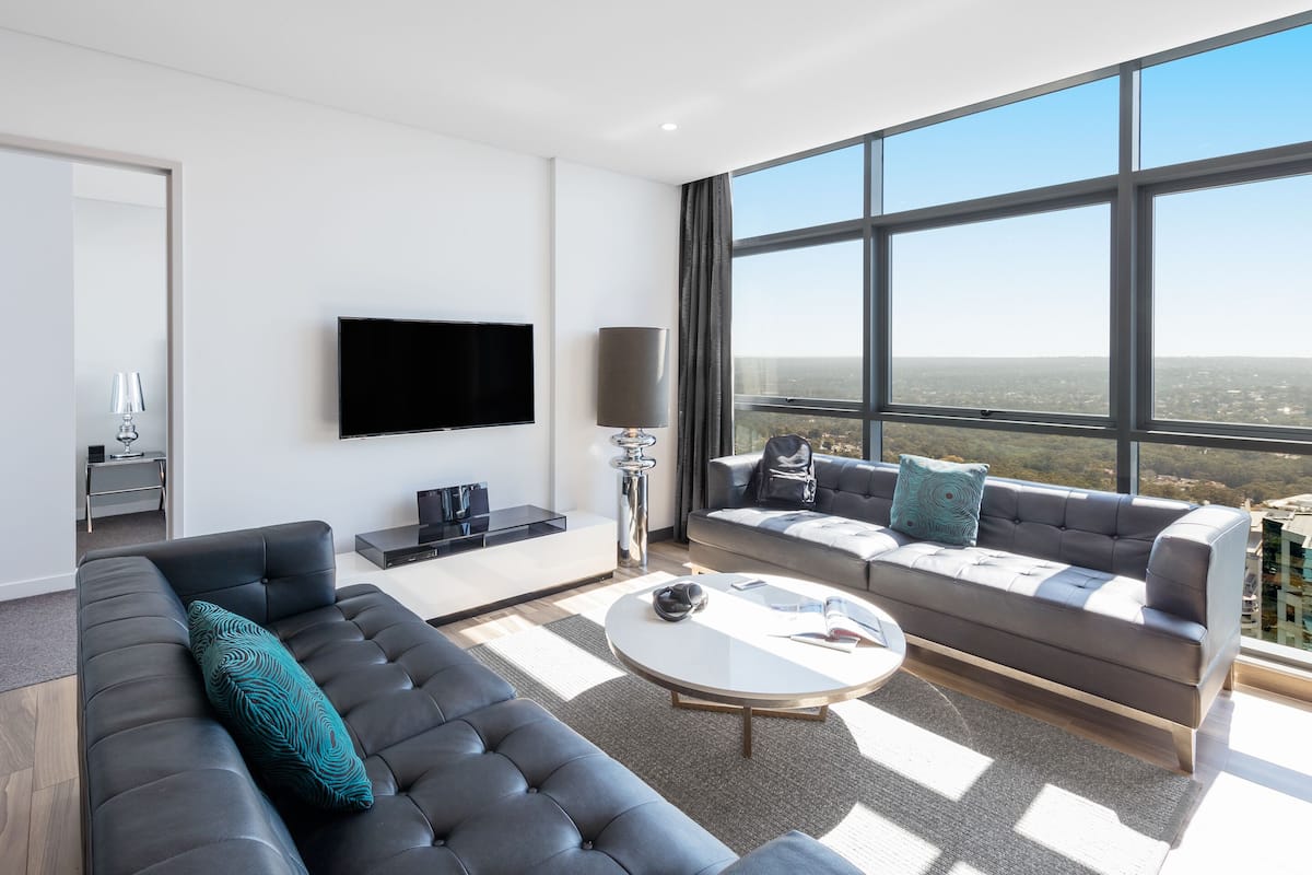 A modern living room with a large window, a flat-screen TV, and a sofa with patterned cushions.