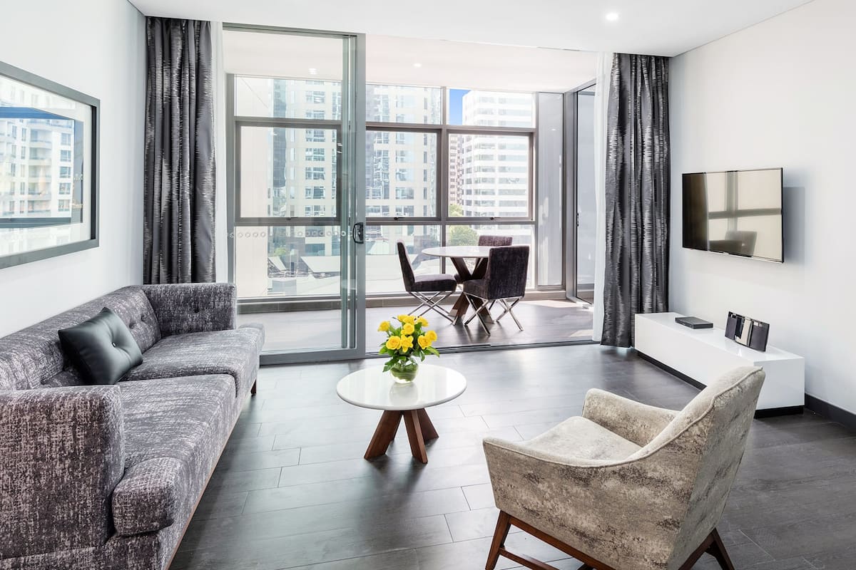 A modern living room with a sofa, armchair, coffee table, and a TV mounted on the wall.