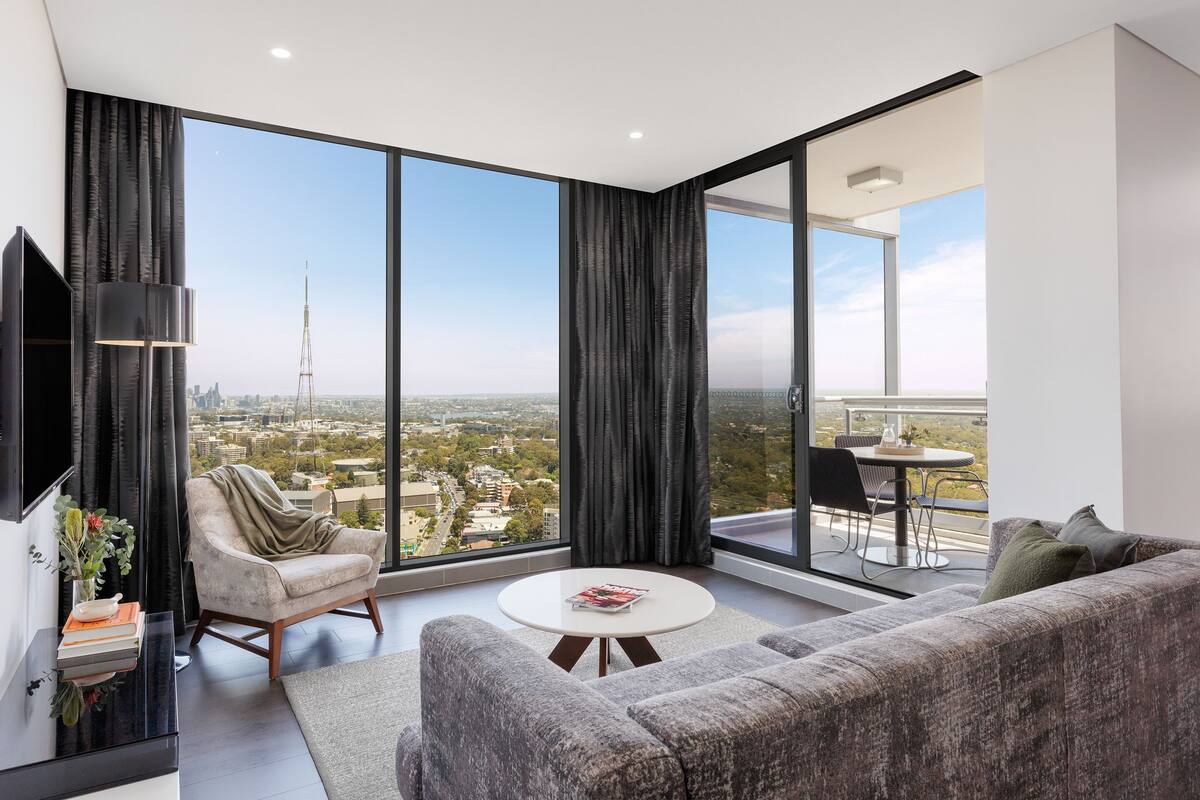 A modern living room with a large window, a sofa, a coffee table, and a chair.