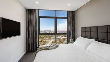 A modern hotel room with a large bed, a flat-screen TV, and a city view through large windows.