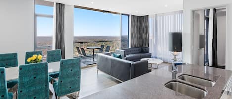 A modern hotel room with a kitchen area, dining space, and a balcony with a city view.