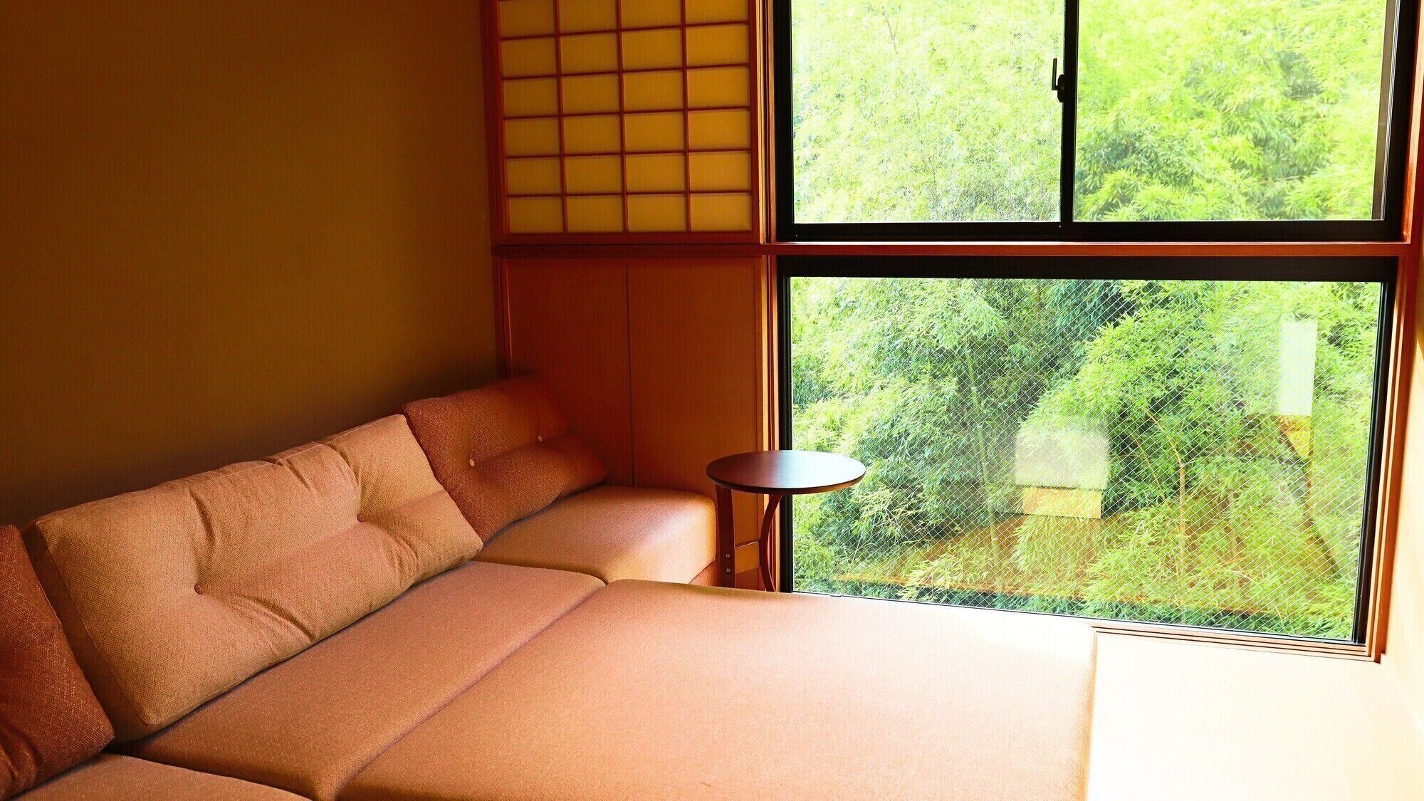A room with a sofa, a small round table, and a large window with a view of greenery.