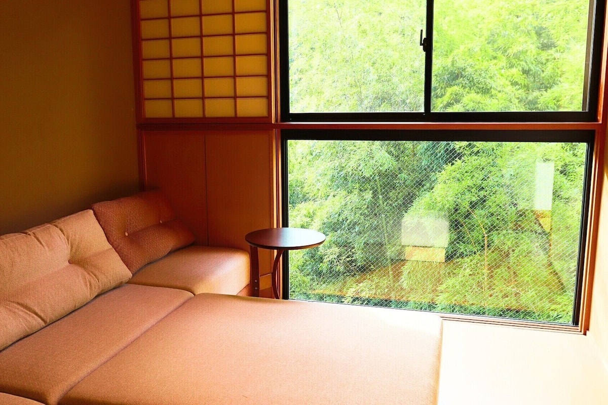 A room with a sofa, a small round table, and a large window with a view of greenery.
