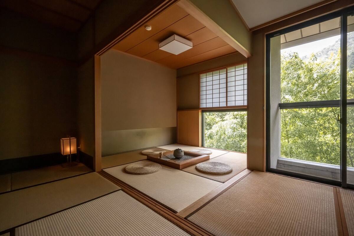 A traditional Japanese room with tatami flooring, a shoji screen, and a view of greenery outside.