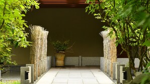 Un sendero que lleva a una estructura tradicional japonesa, con piso de baldosas y decoraciones de bambú.