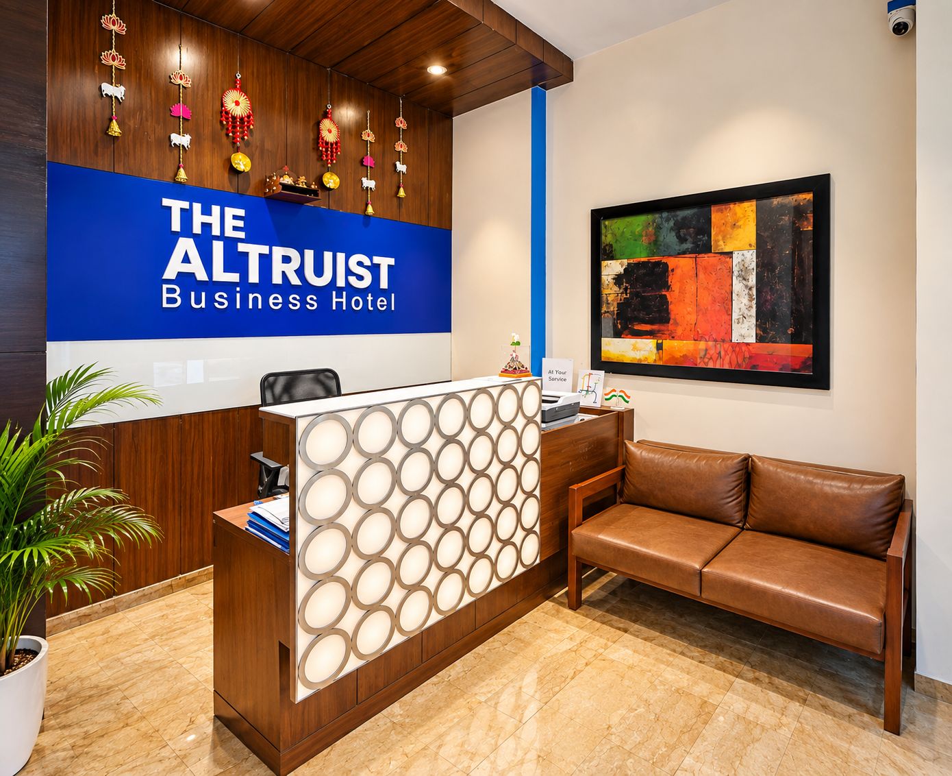 A reception desk with a blue sign reading 'The Altruist Business Hotel,' a modern abstract painting on the wall, and a leather sofa in the lobby area.