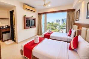 A hotel room with two beds, a TV, an air conditioning unit, a desk with a kettle, and a view of the city. - The Altruist Andheri Hotel (Mumbai)