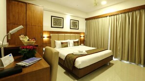 Habitación de hotel con cama, escritorio con lámpara, cesta de frutas y un jarrón de flores.