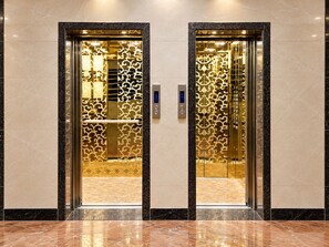 A pair of elevator doors with a decorative golden pattern, a control panel, and a marble floor. - The Altruist Andheri Hotel (Mumbai)