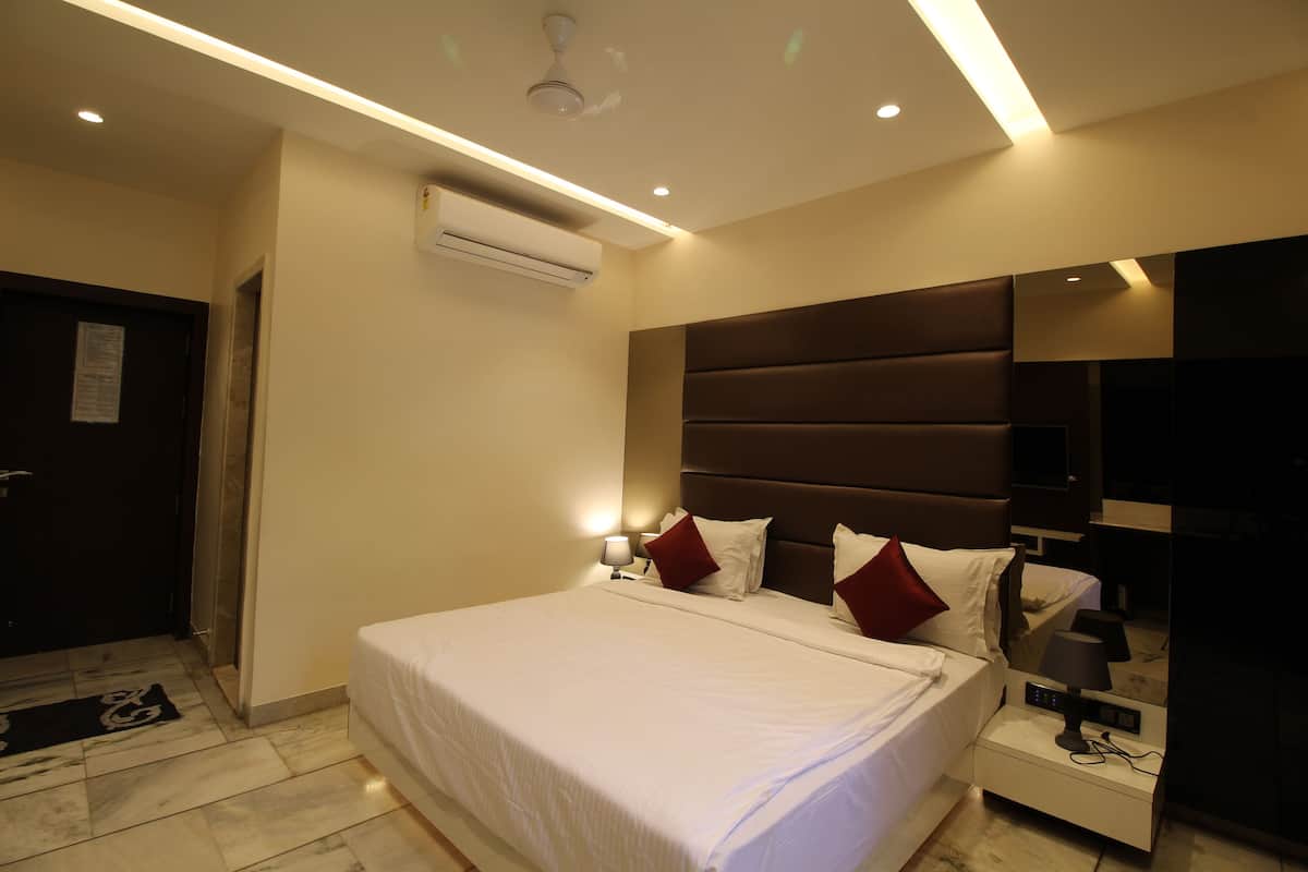 A modern hotel room with a large bed, bedside lamps, a flat-screen TV, and an air conditioning unit.