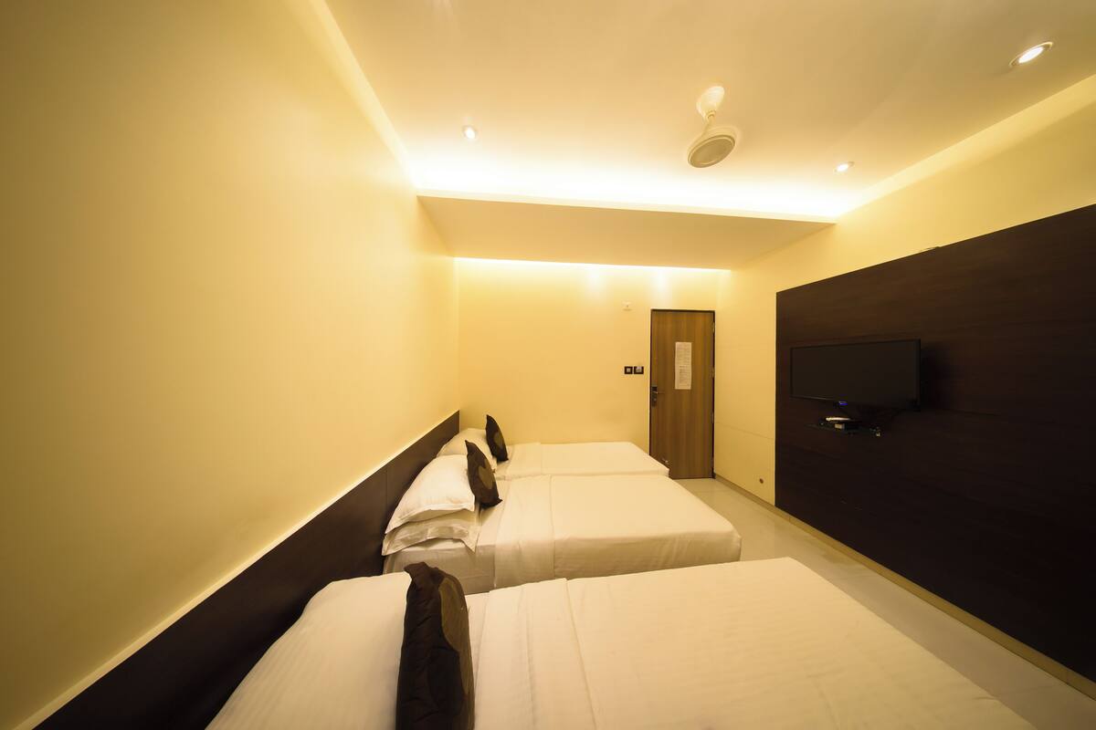 A hotel room with two beds, a television on the wall, and a door in the background.