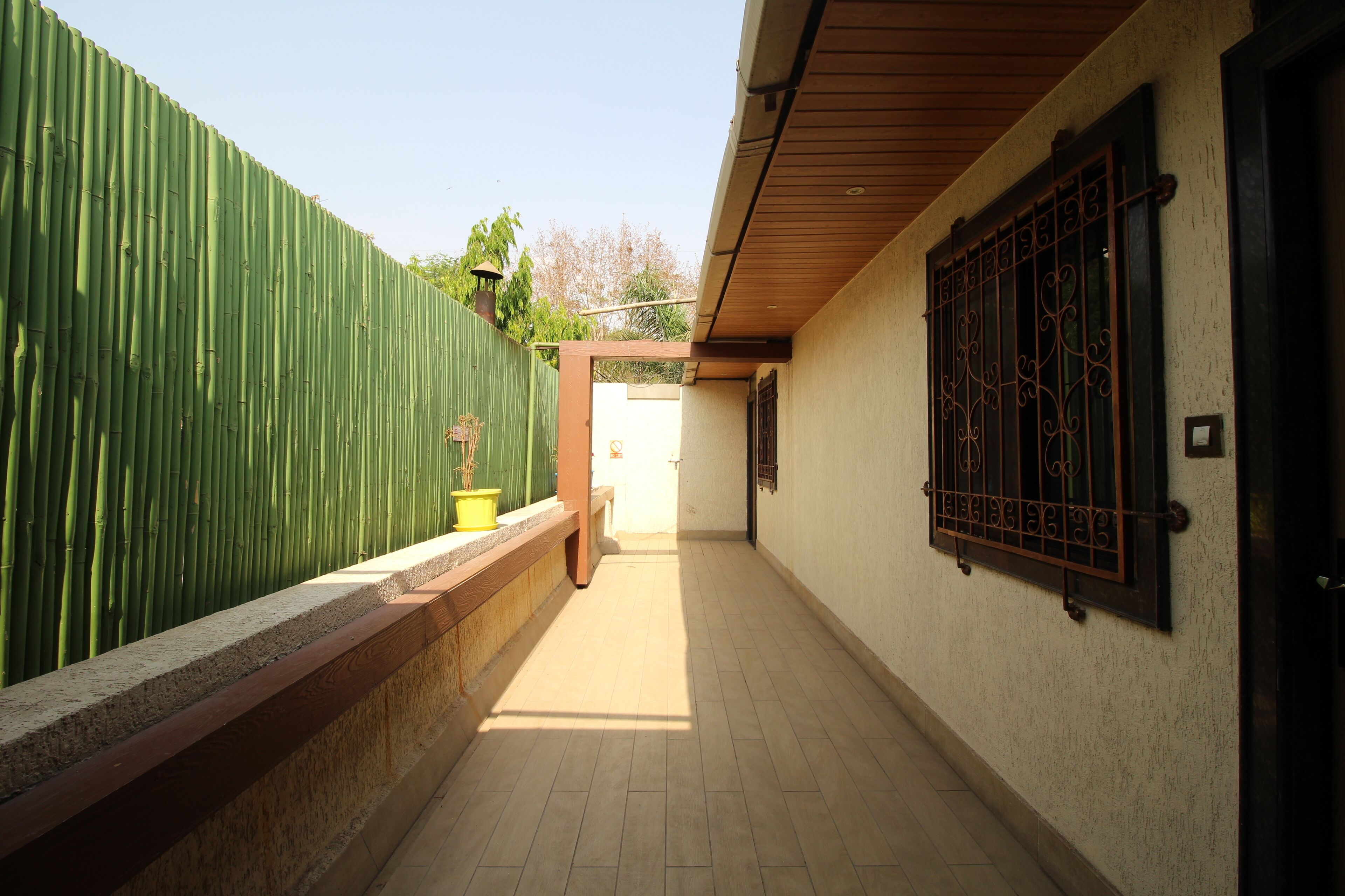 A corridor with a green bamboo fence, a wooden bench, and a door at the end.