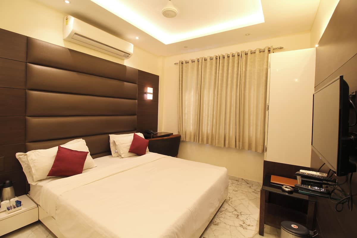 A hotel room with a large bed, a flat-screen TV, a desk with a computer, and an air conditioning unit.
