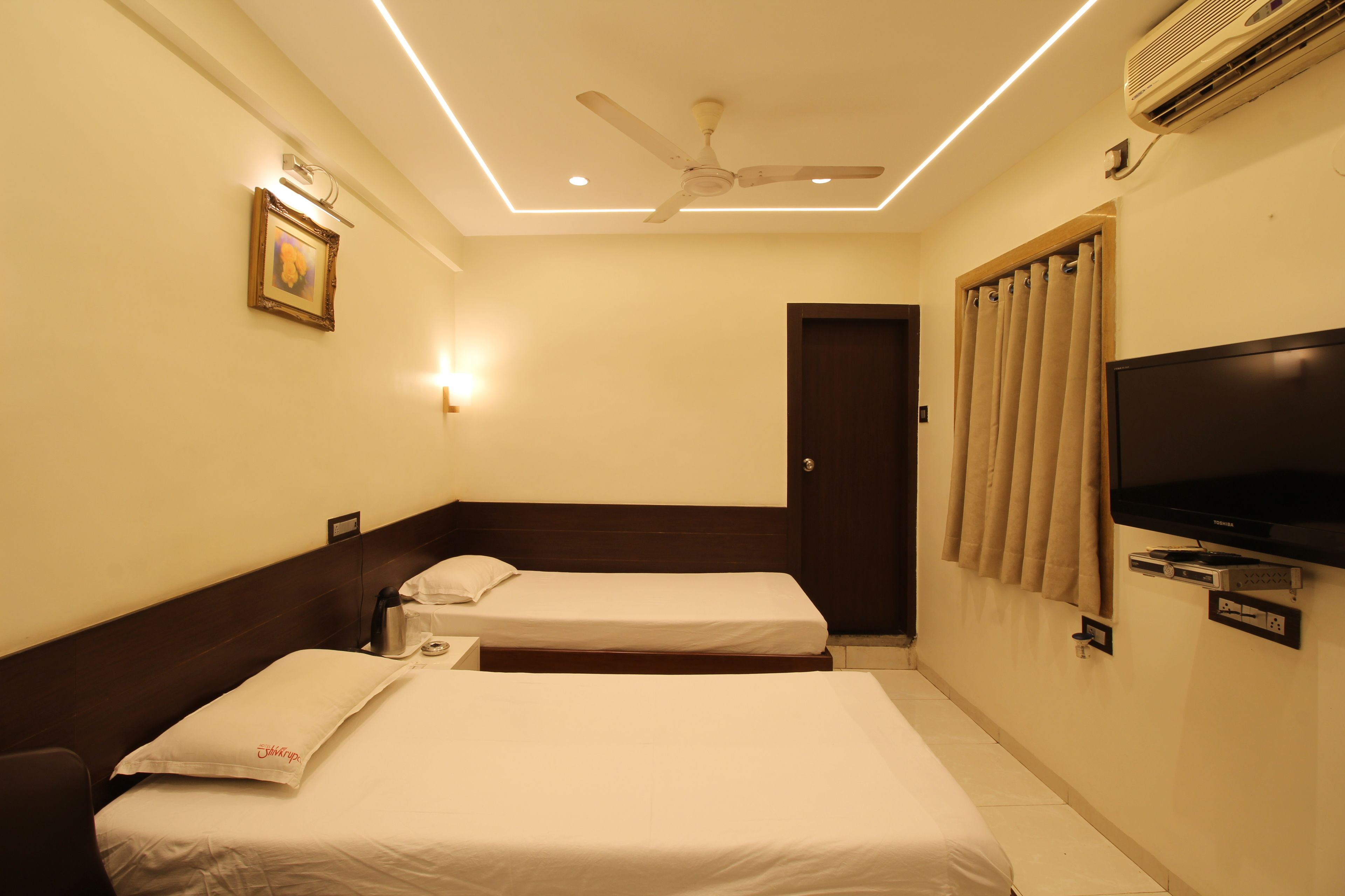 A hotel room with two beds, a ceiling fan, a flat-screen TV, and an air conditioning unit.