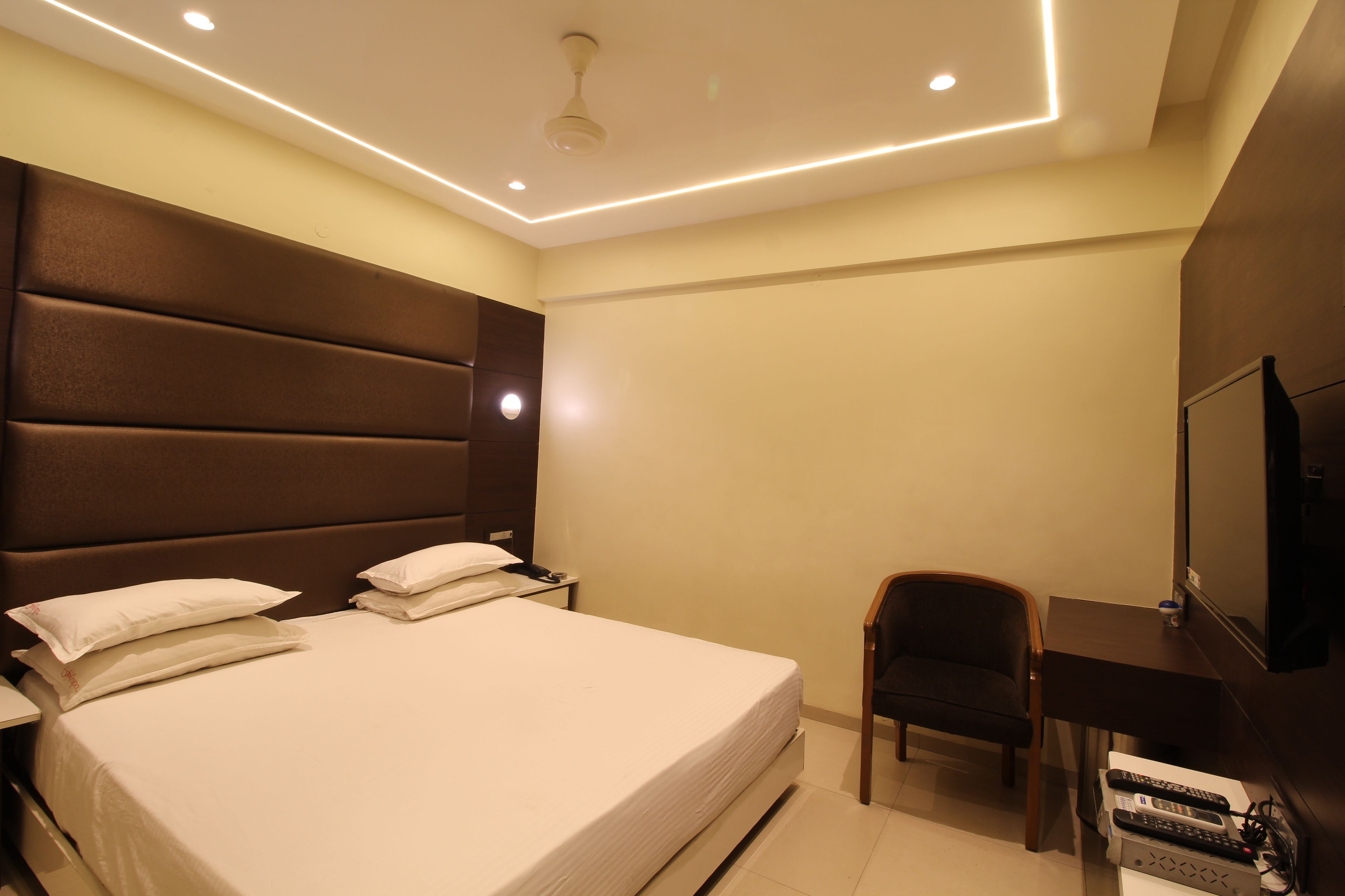 Una habitación de hotel con una cama grande, un escritorio con silla, un televisor y un panel de control.