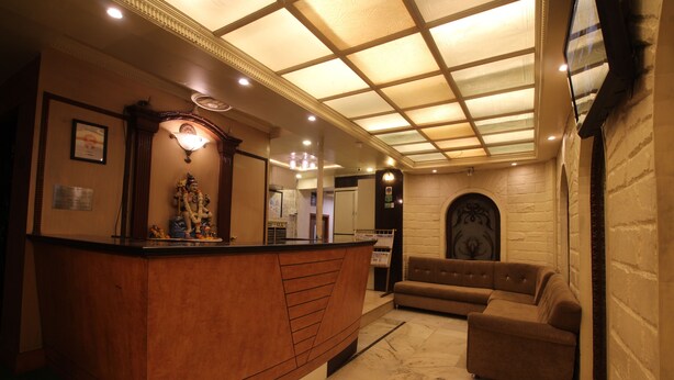 A reception area with a wooden counter, a sofa, and a ceiling with a grid pattern. - Hotel Shivkrupa (Pune)