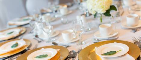 Una mesa dispuesta para un evento gastronómico formal, con vajilla y cubertería blancos y dorados, incluyendo platos, copas y cubiertos.