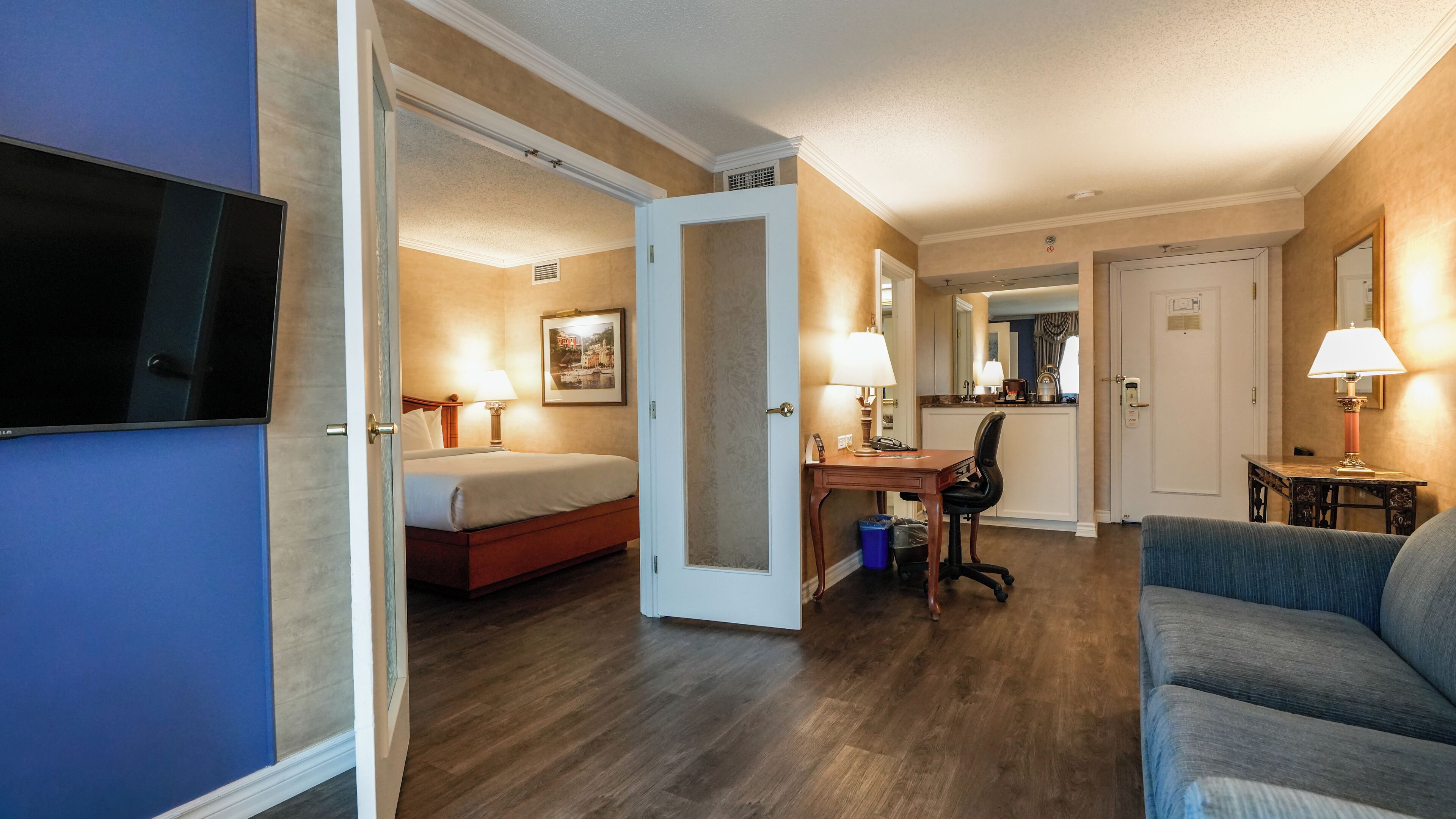 Quarto de hotel com cama, escrivaninha, cadeira e televisão.
