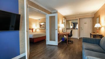 Quarto de hotel com cama, escrivaninha, cadeira e televisão.