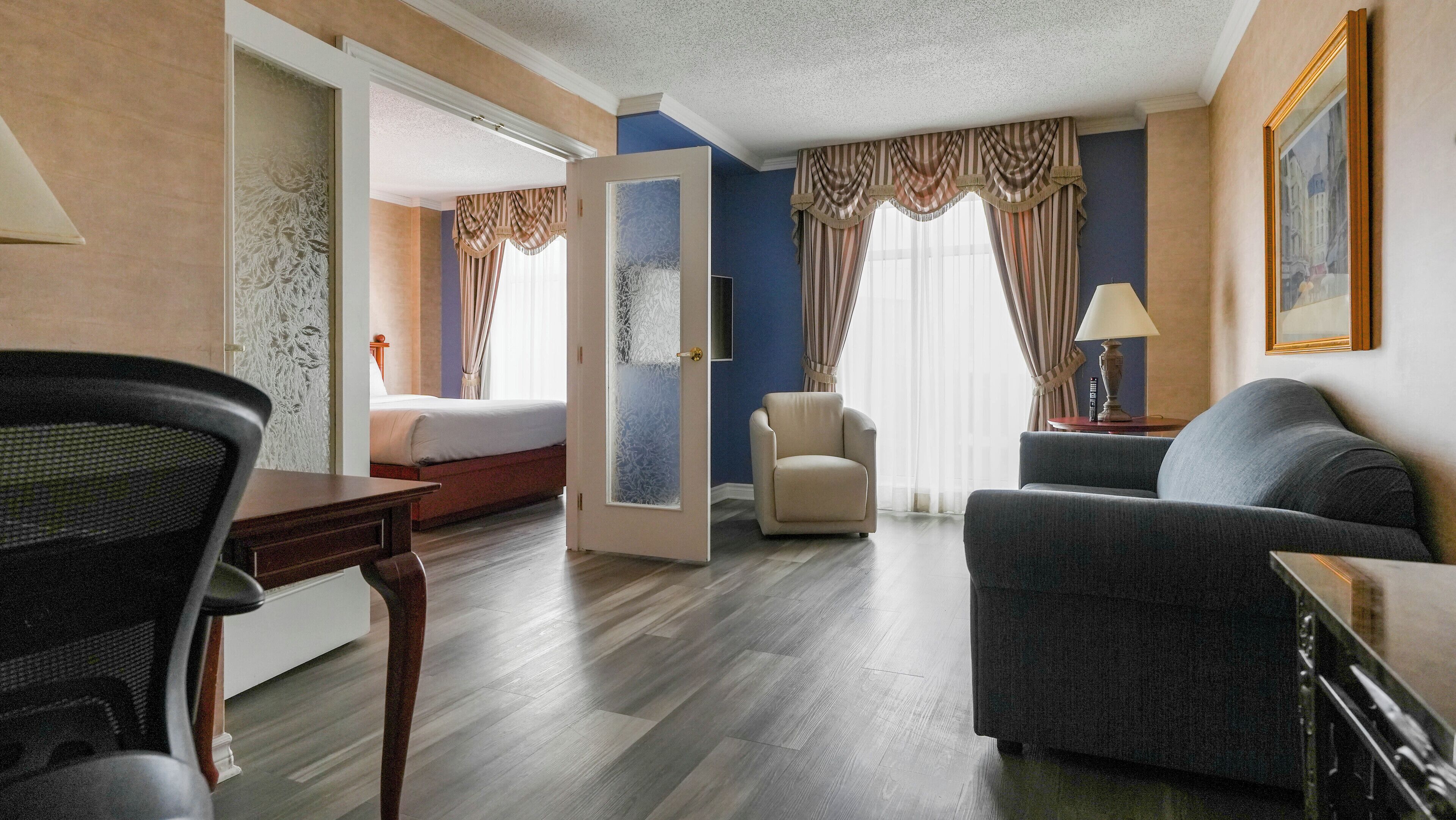 A hotel room with a bed, a desk, a chair, a sofa, and a lamp.
