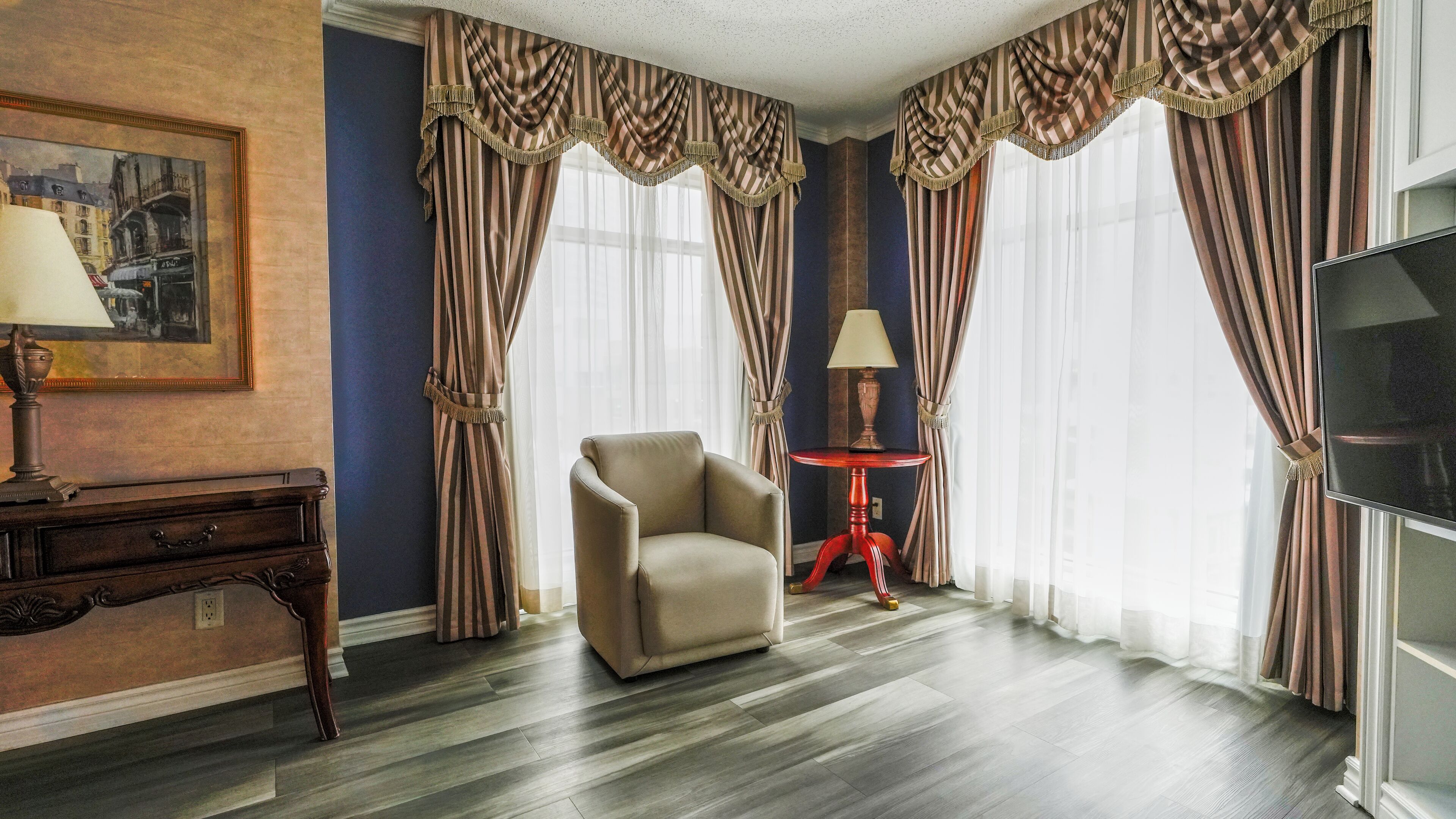 Una habitación con cortinas a rayas, un sofá, una mesa con una lámpara y un cuadro en la pared.