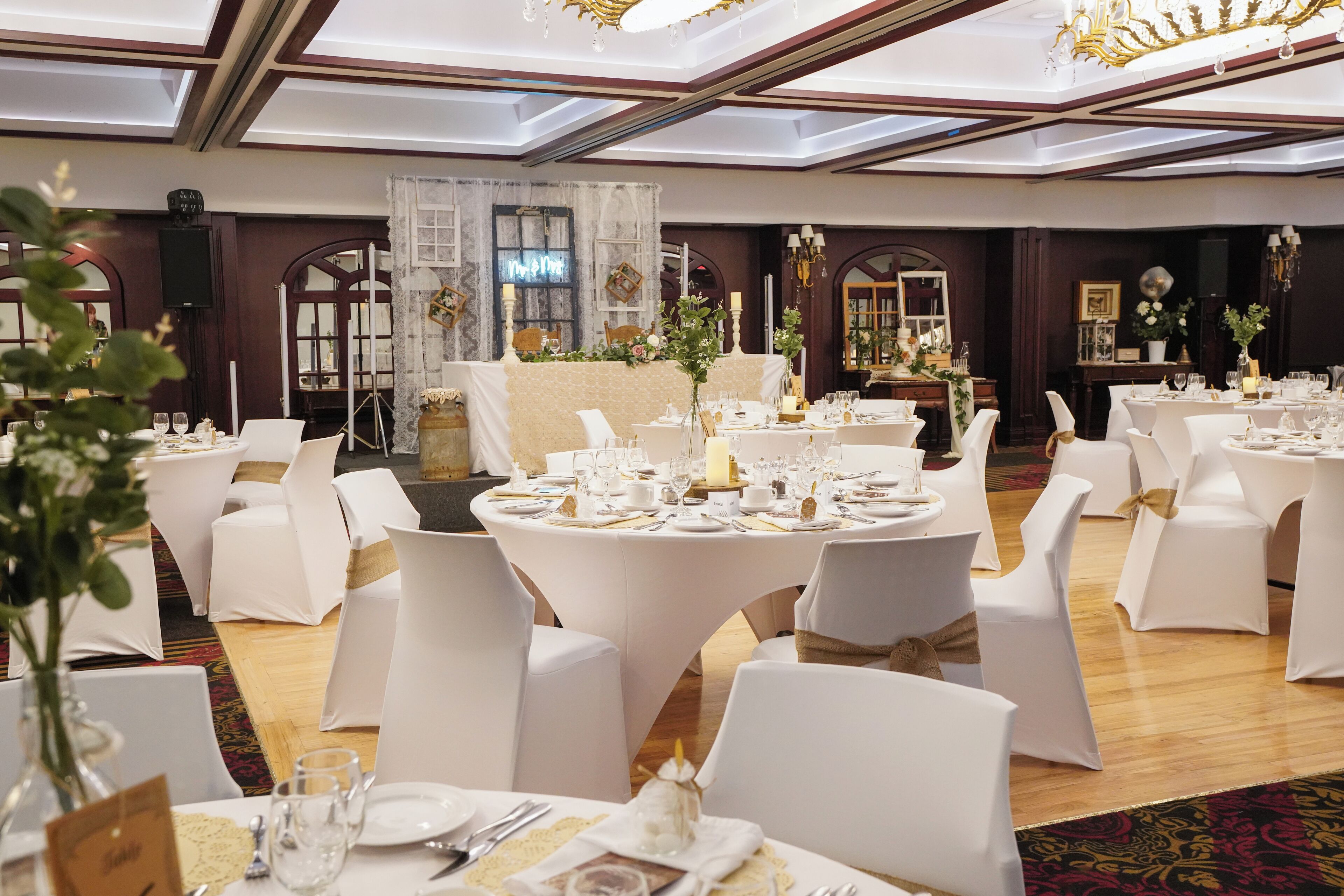 Uma sala de banquetes com mesas redondas preparadas para um evento formal, com toalhas brancas, cadeiras e centros de mesa florais.