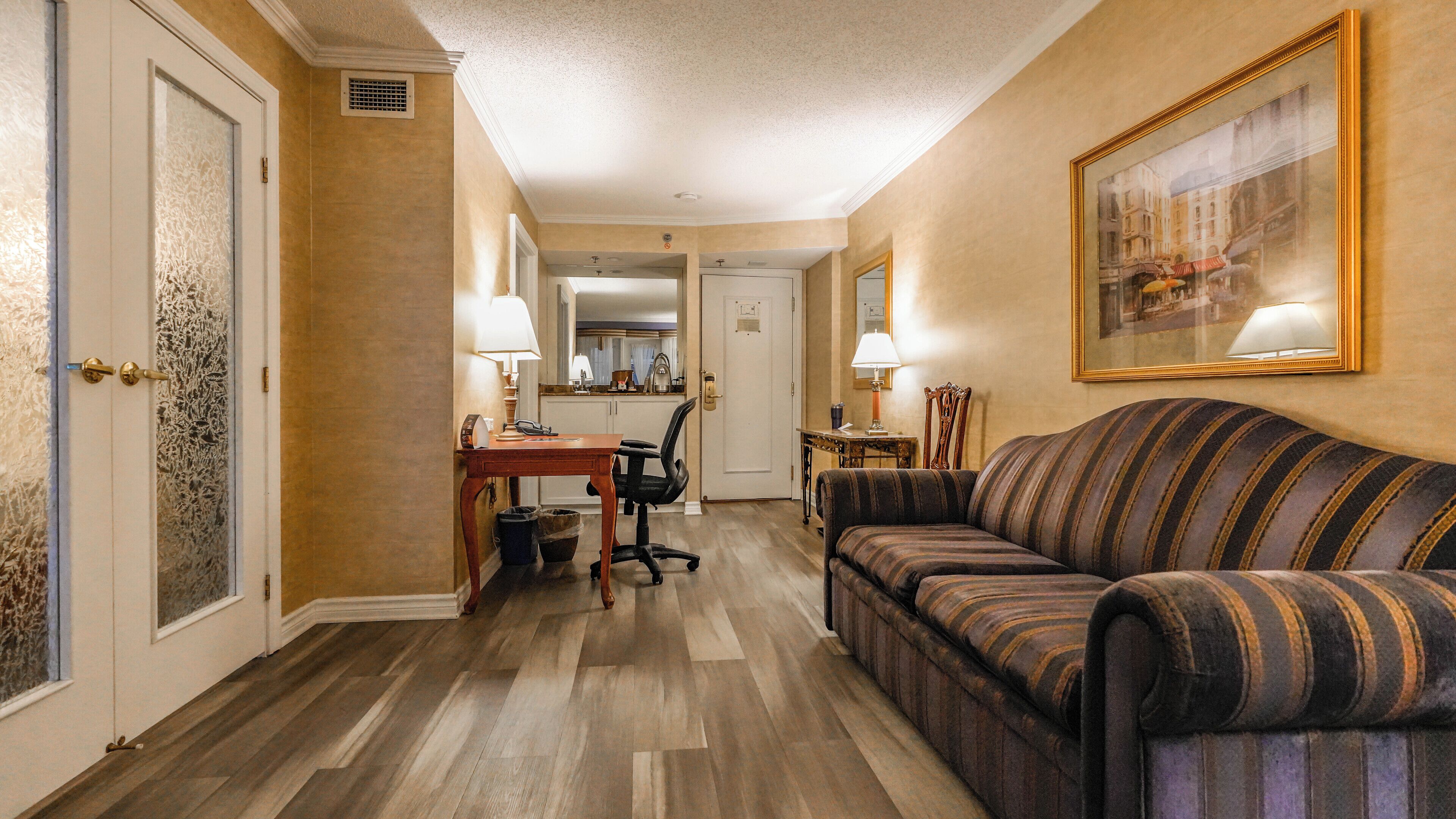 Une chambre d’hôtel avec un plancher en bois, un canapé à rayures, un bureau avec une chaise et un coin repas.