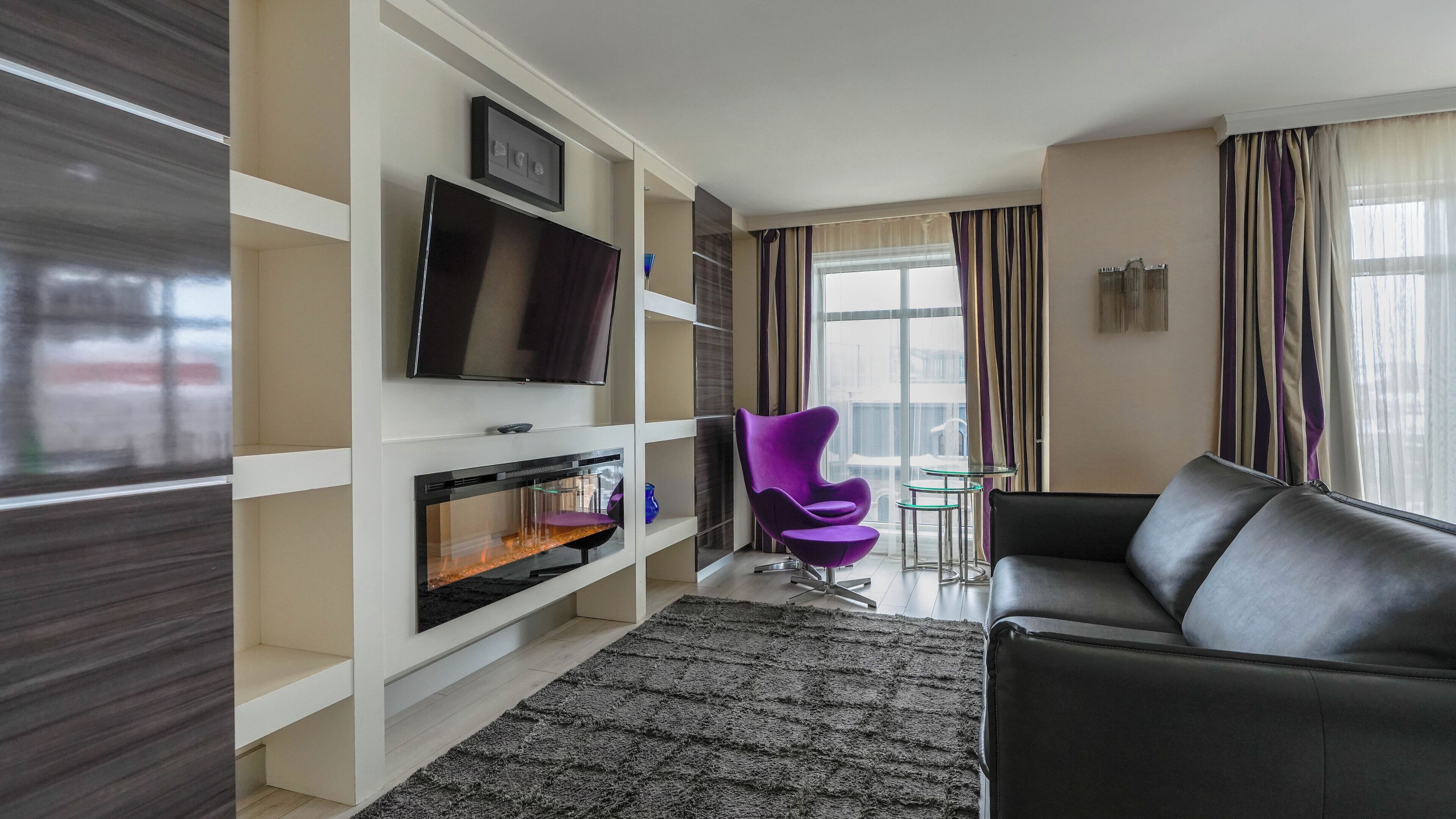 Een moderne woonkamer met een flatscreentelevisie, een open haard, een paarse stoel en een zwarte bank.