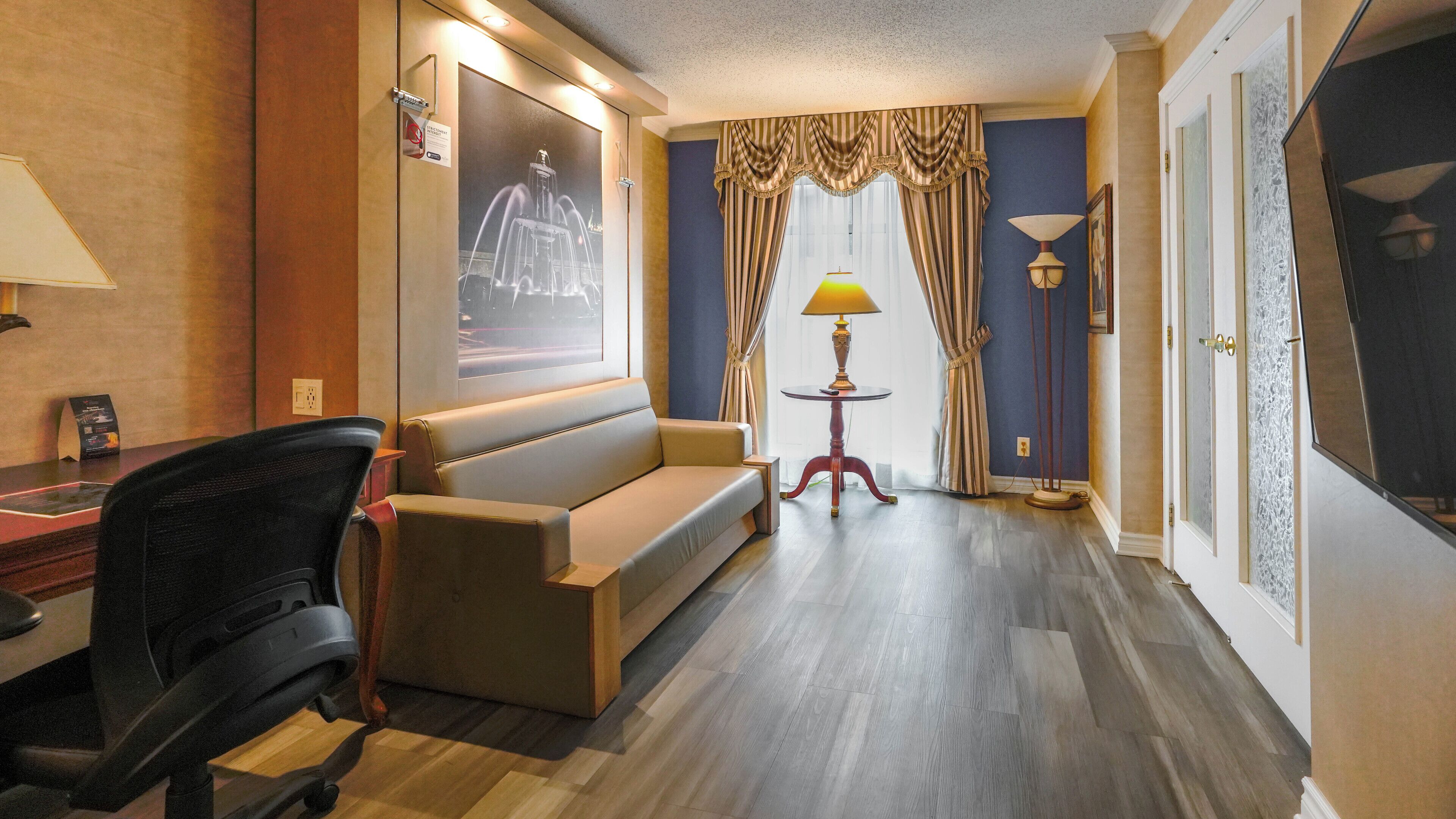 Habitación de hotel con sofá, escritorio, silla, lámpara y un cuadro en la pared.