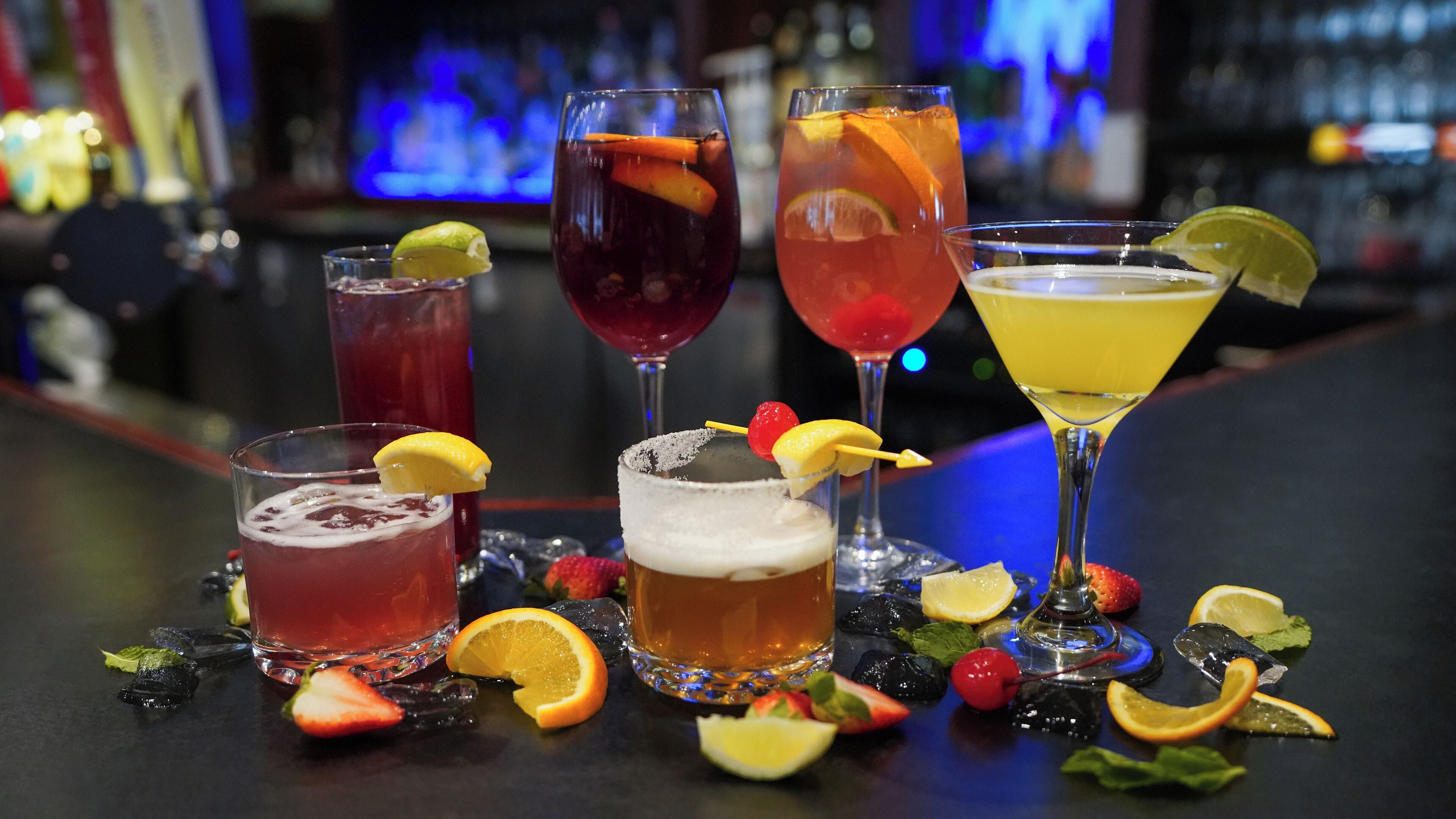 Un bar amb diversos cocktails, guarniments i un fons fosc amb il·luminació blava.