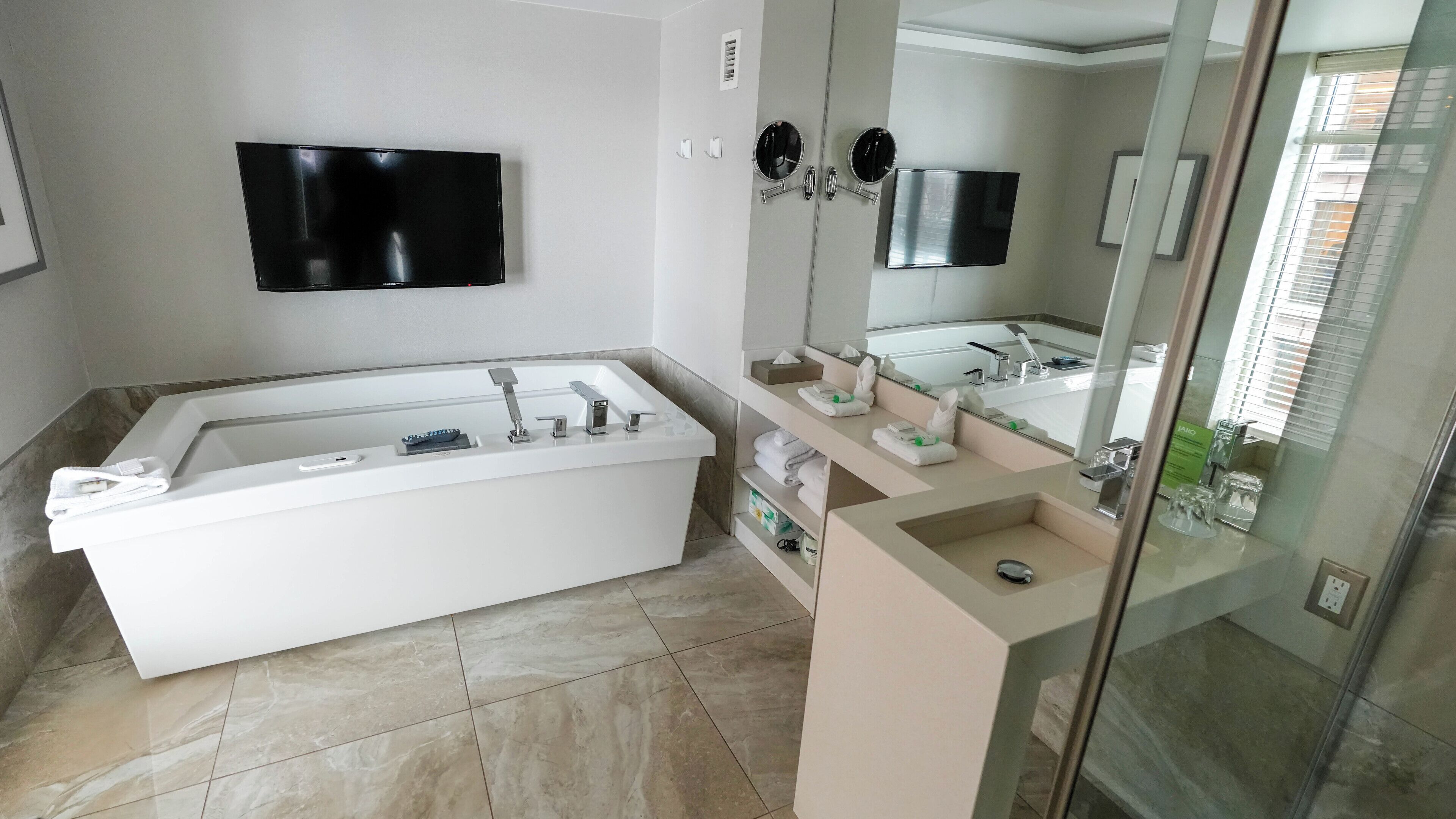 Un baño moderno con una bañera grande, un tocador con espejo y un televisor de pantalla plana montado en la pared.