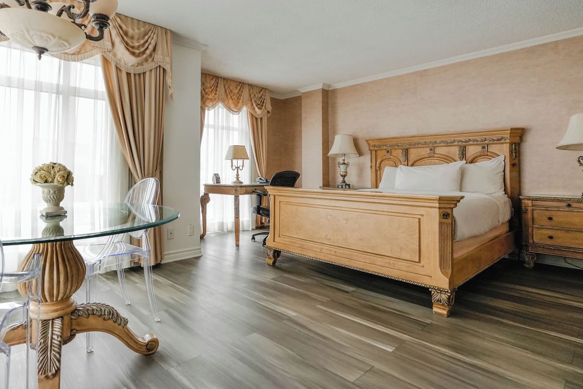 Ett hotellrum med en stor säng, ett glasbord, en stol, ett skrivbord och en lampa.