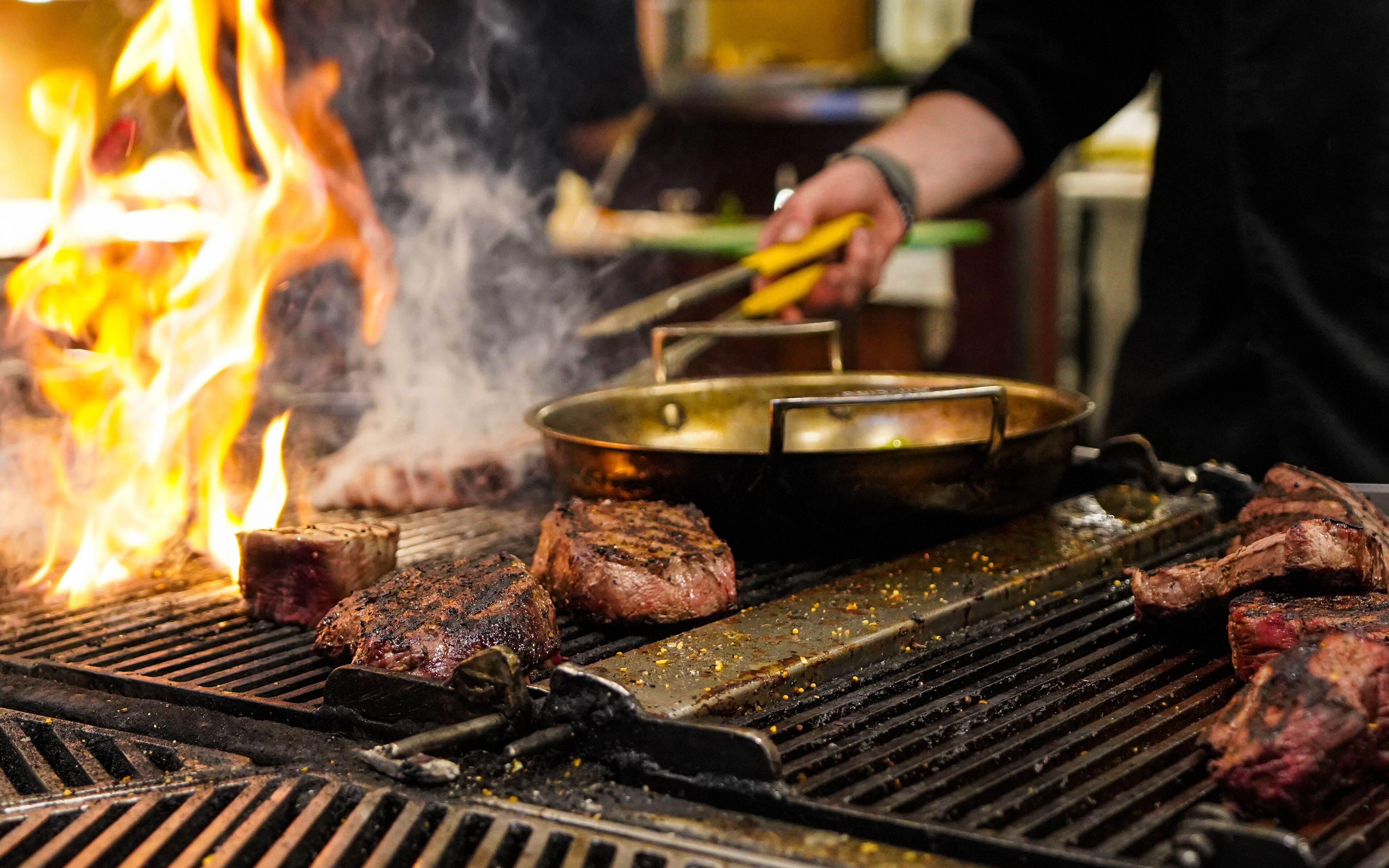 Un gril sur lequel plusieurs steaks sont en train de cuire au-dessus d’une flamme nue.