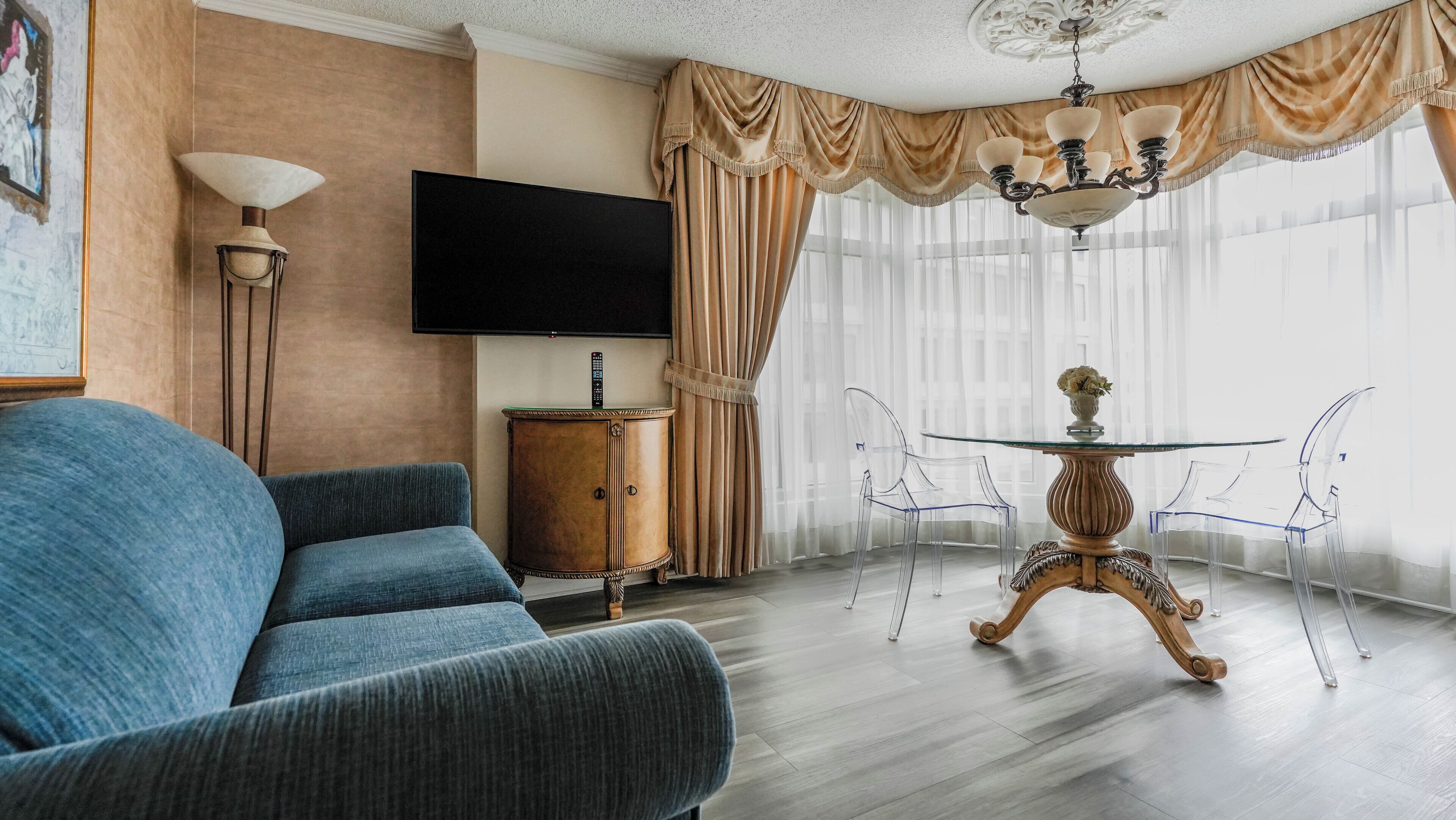 A living room with a blue sofa, a wooden cabinet, a flat-screen TV, a chandelier, and a glass table with chairs.
