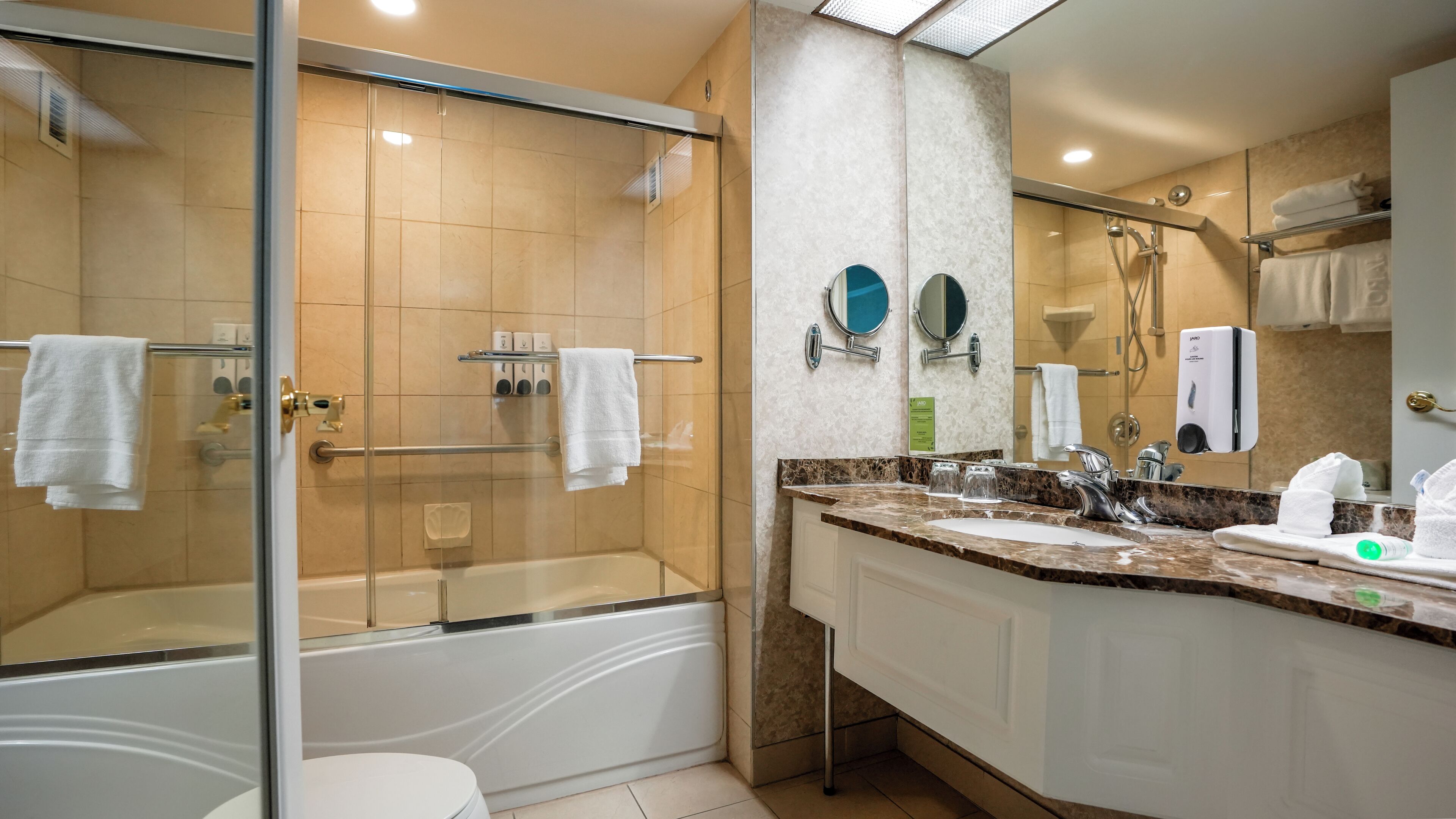 A modern bathroom with a glass-enclosed shower, a white bathtub, and a marble countertop with a sink and mirror.