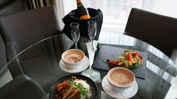 A dining table with a bottle of champagne, two glasses, and two cups of coffee. There is a plate of food and a dessert on the table.