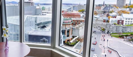 A corner room with a large window overlooking a cityscape, including historic buildings and a waterfront.