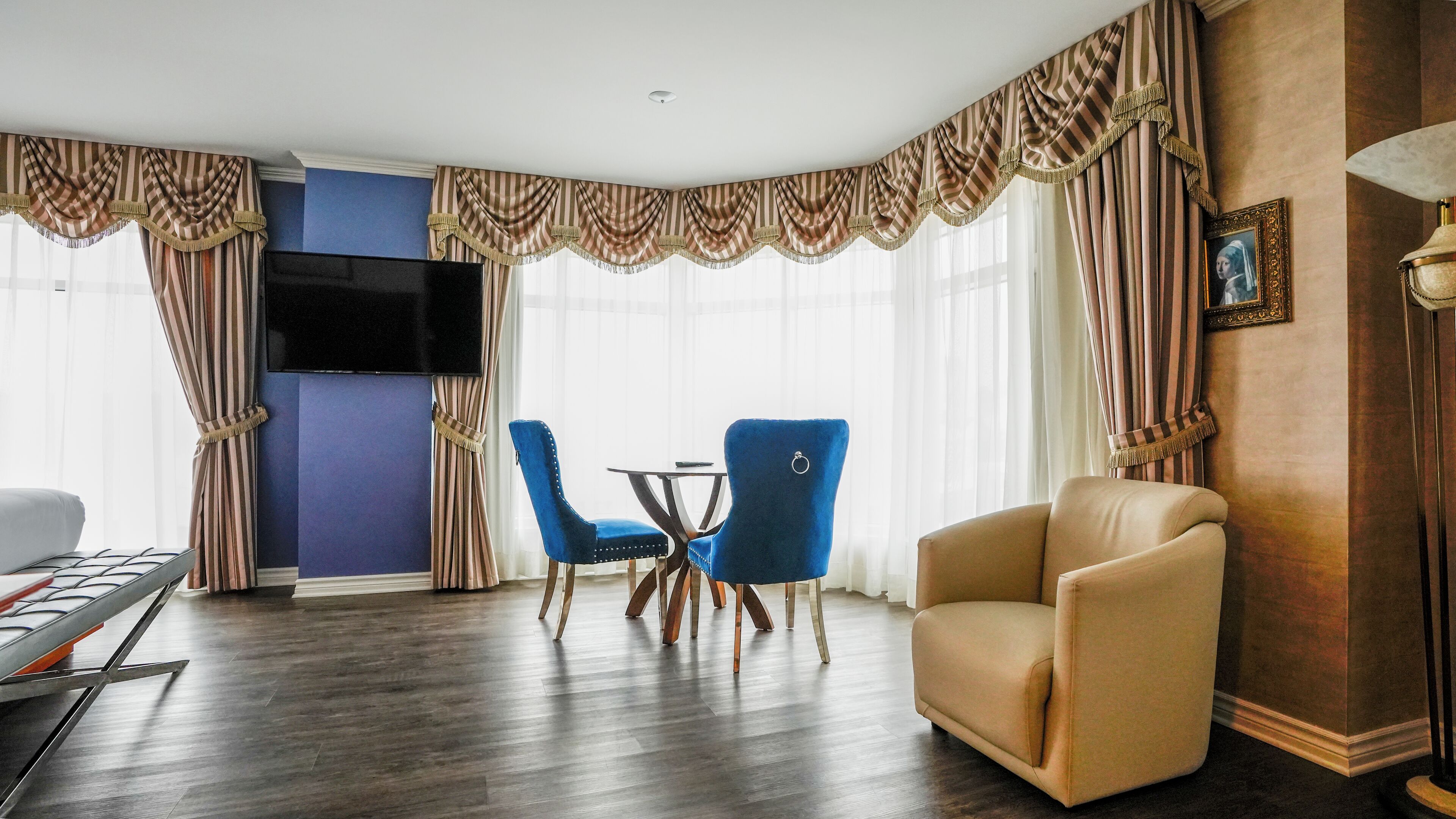 Ein Hotelzimmer mit Flachbildfernseher, zwei blauen Stühlen, einem beigen Sessel, einem kleinen Tisch und einer Lampe.